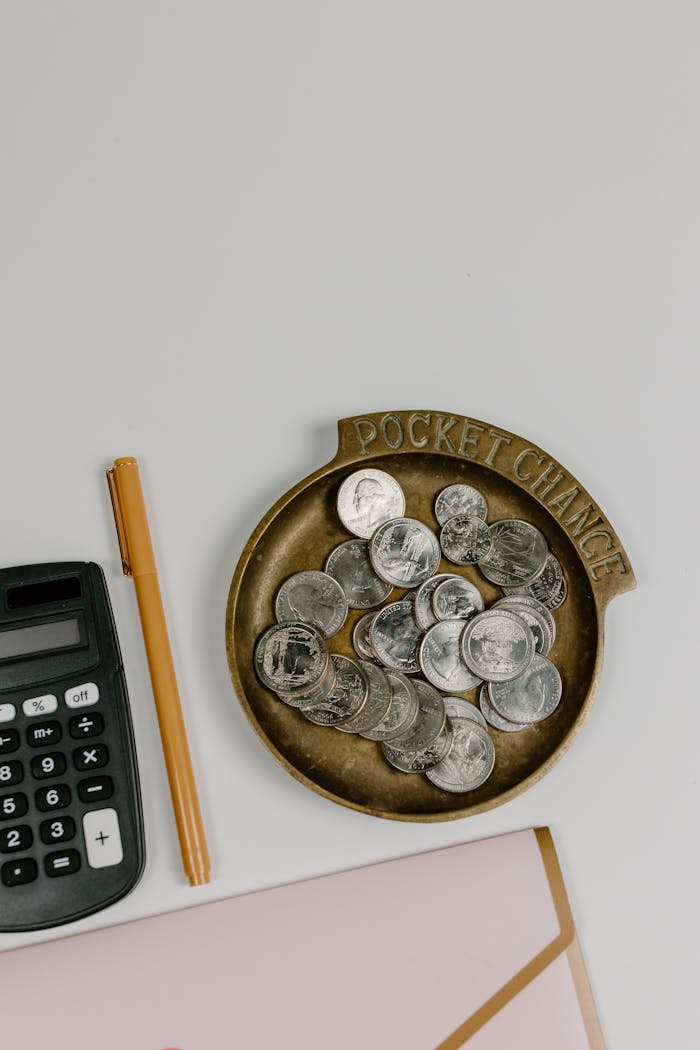 Top-down view of coins, calculator, and pen on a white surface, ideal for finance concept.